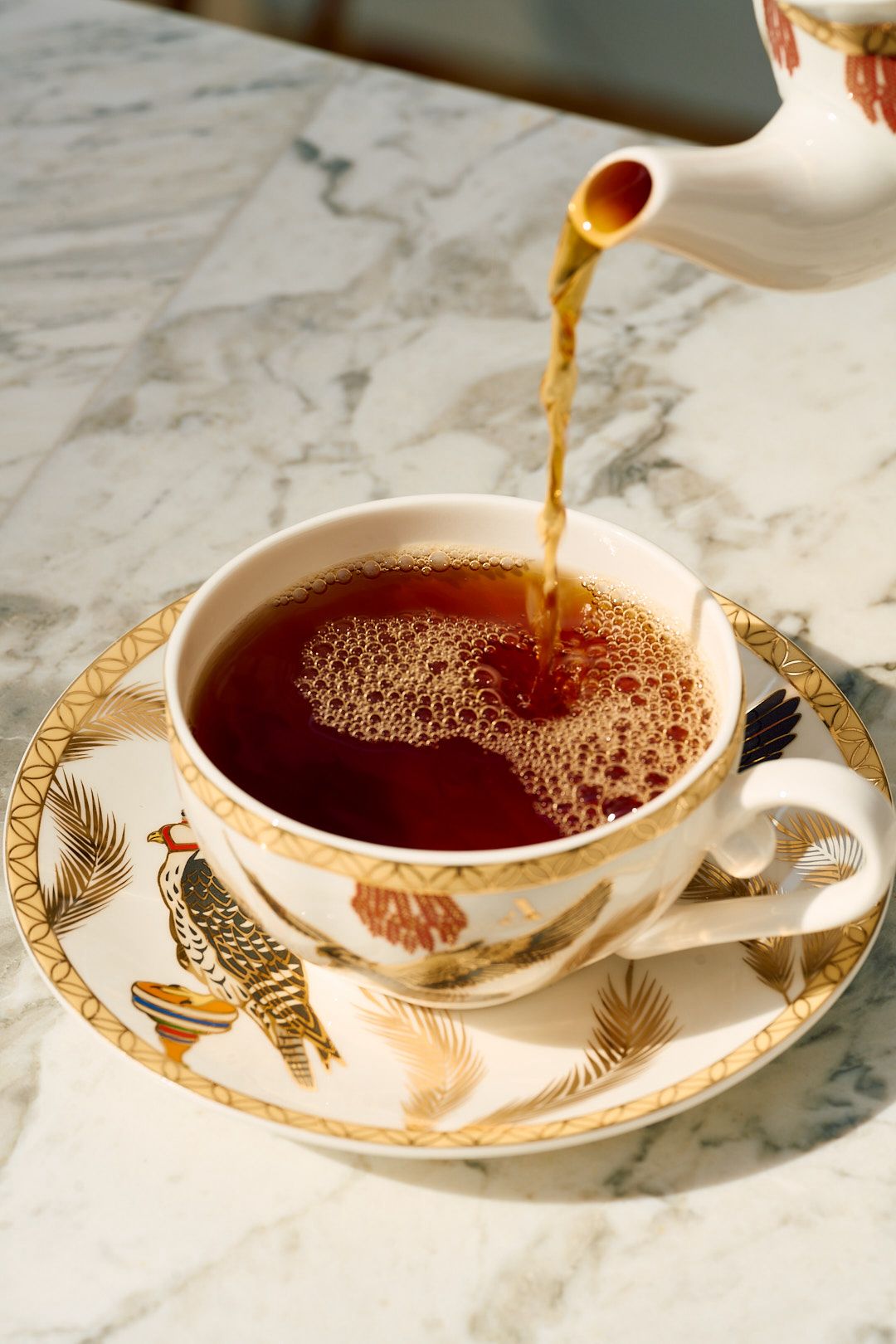 Tea poured from a porcelain spout into a gilded Al-Bidaa cup on marble